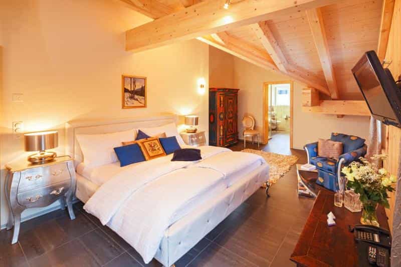 Bedroom with white bedding, exposed wood beams, and colorful antique wardrobe in Griesalp.