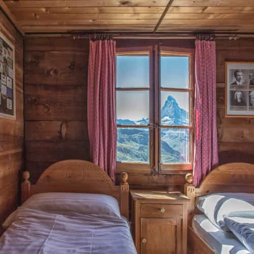 Hut interior with wooden walls, beds, and window view of the Matterhorn peak.