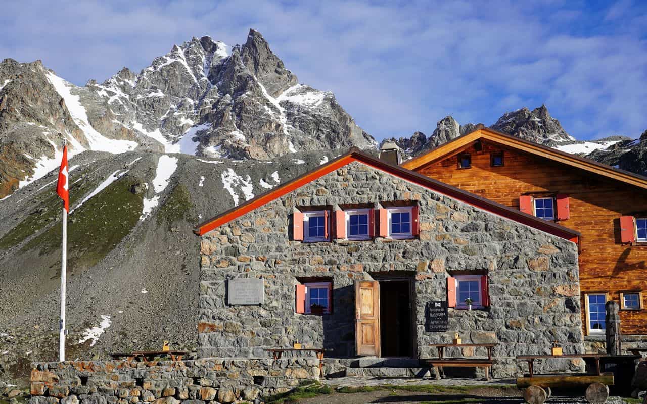 Stone and wood alpine hut with Swiss flag below snow-capped mountains