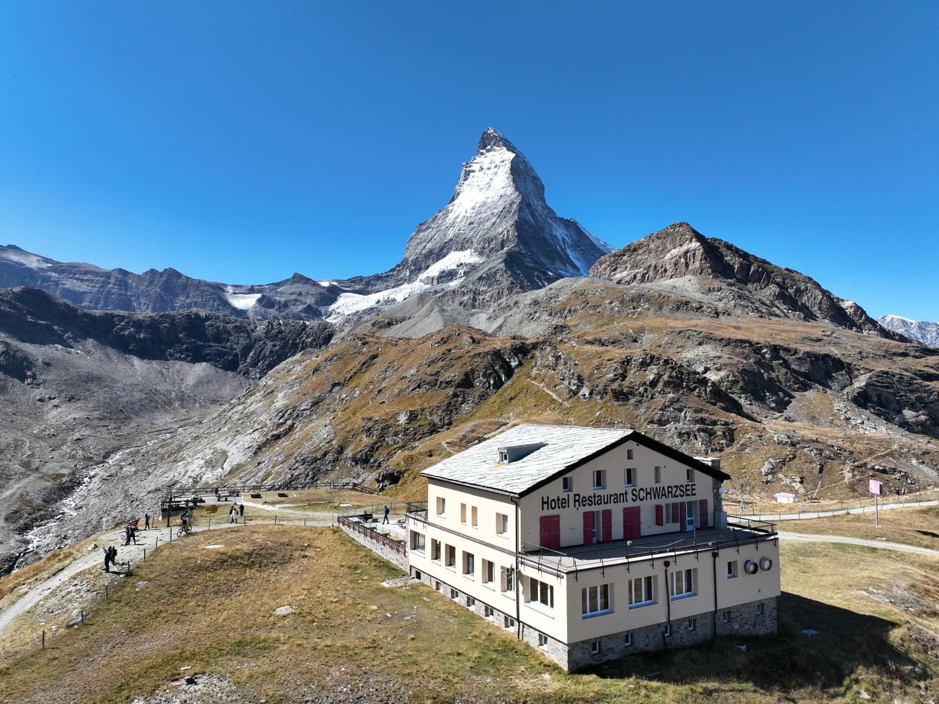 Hotel Restaurant Schwarzsee with snow-capped Matterhorn peak in the background under a clear blue sky.