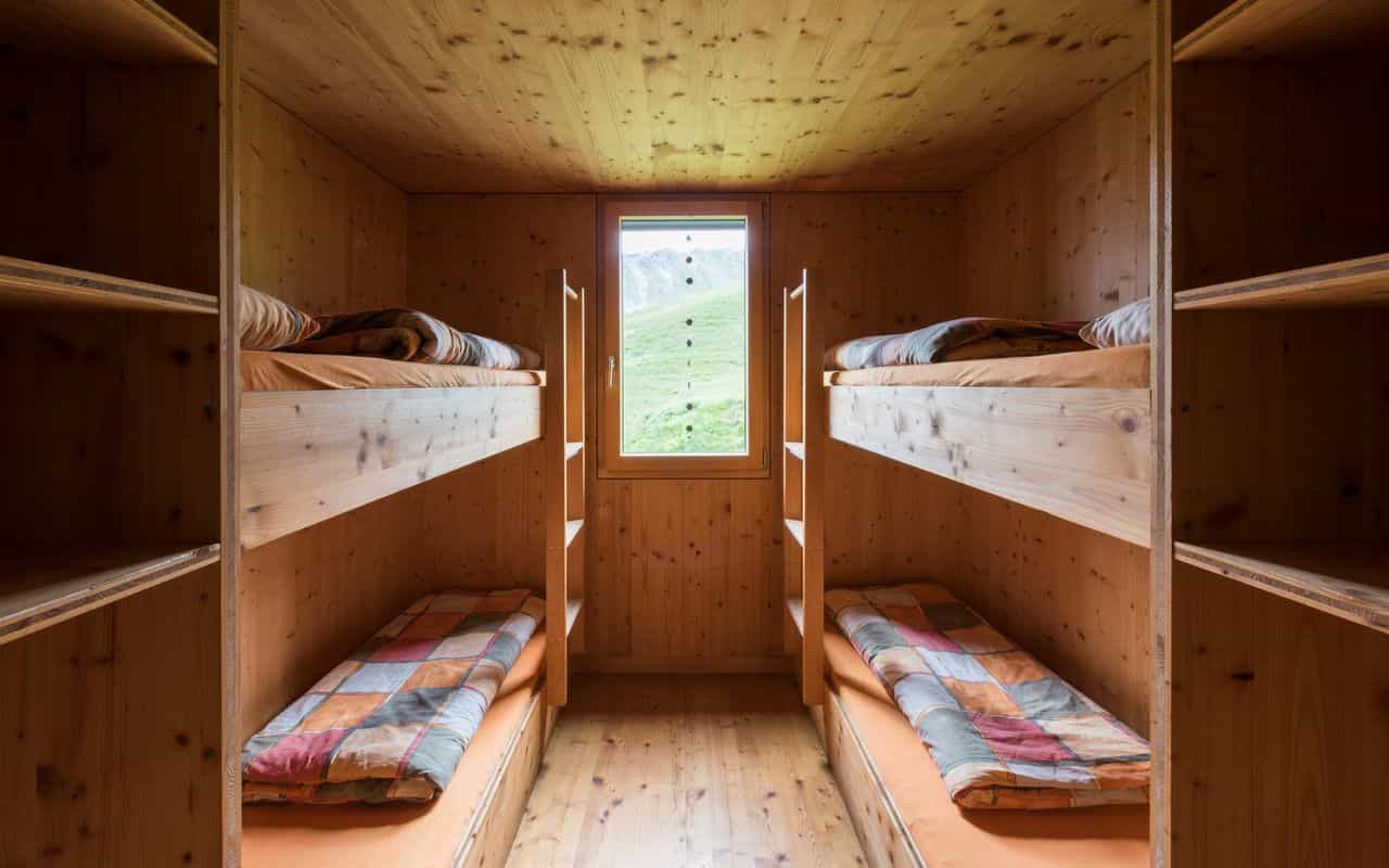 Bunk room with wood paneling, beds, and window view of green mountain slope.