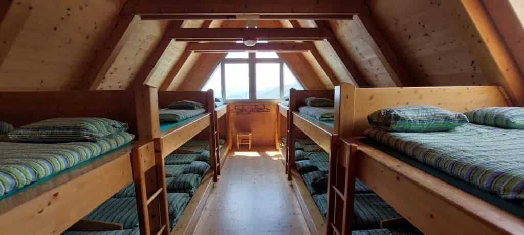 Bunk beds in a wooden alpine hut attic room with a window view of mountains