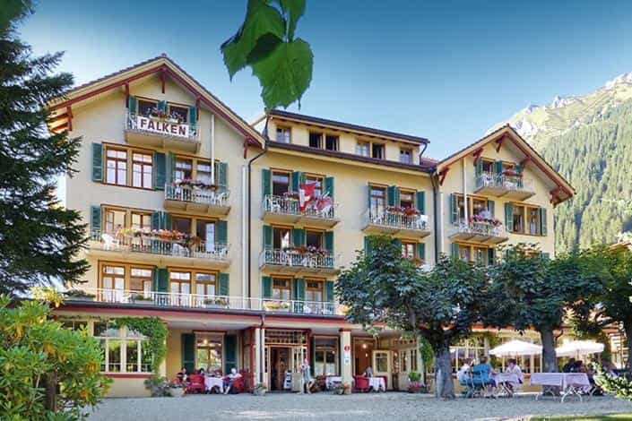 Hotel Falken building with balconies, outdoor dining, and mountain backdrop.