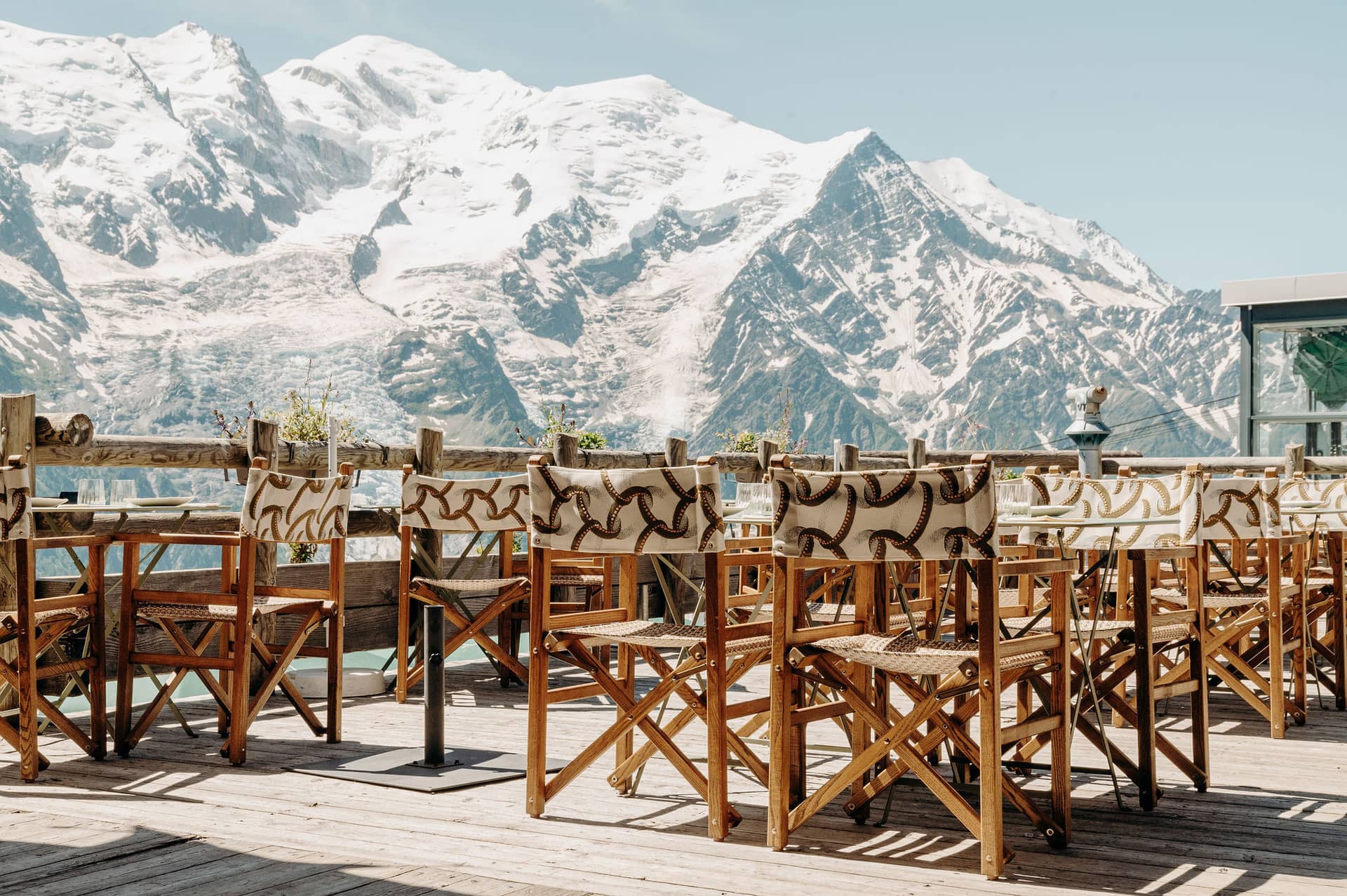 Outdoor restaurant terrace with wooden chairs and tables overlooking snow-capped mountain peaks