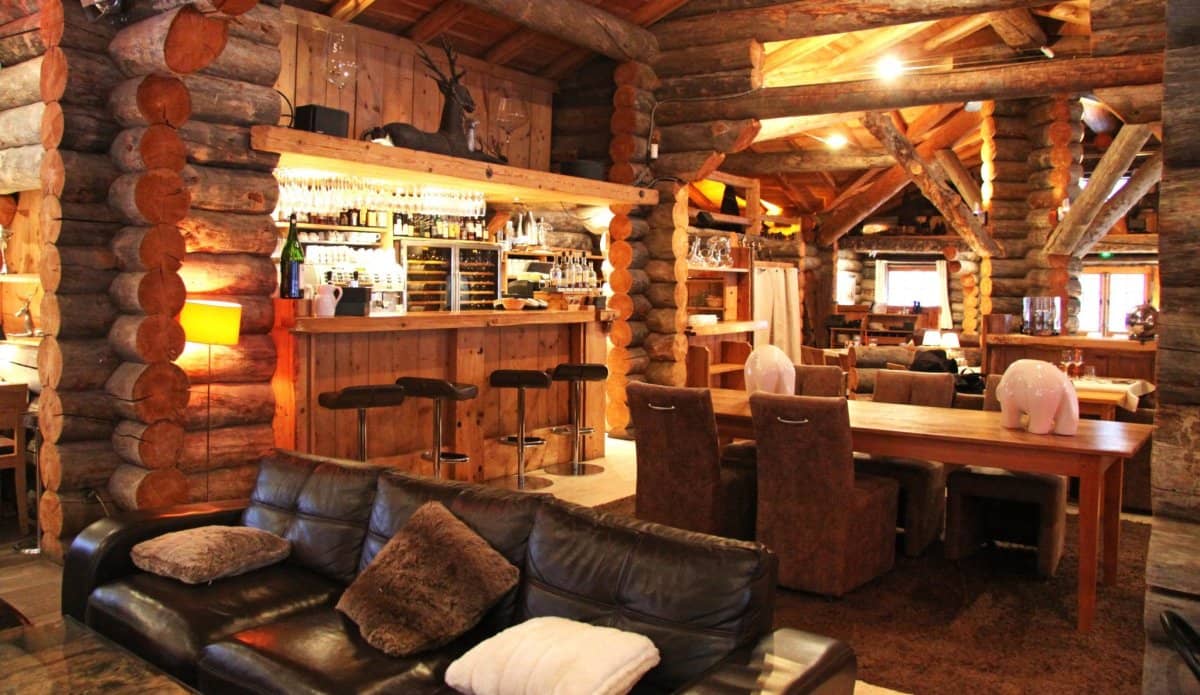 Rustic log cabin interior with wooden bar, dining tables, and leather sofa at La Cabane des Praz