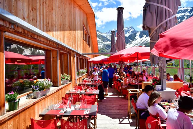 Outdoor terrace dining with red umbrellas at Le Dahu restaurant in front of snowy alpine mountains