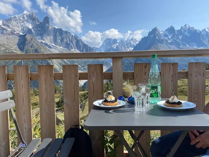 Outdoor table with pastries and drinks on a balcony overlooking snowy mountain peaks