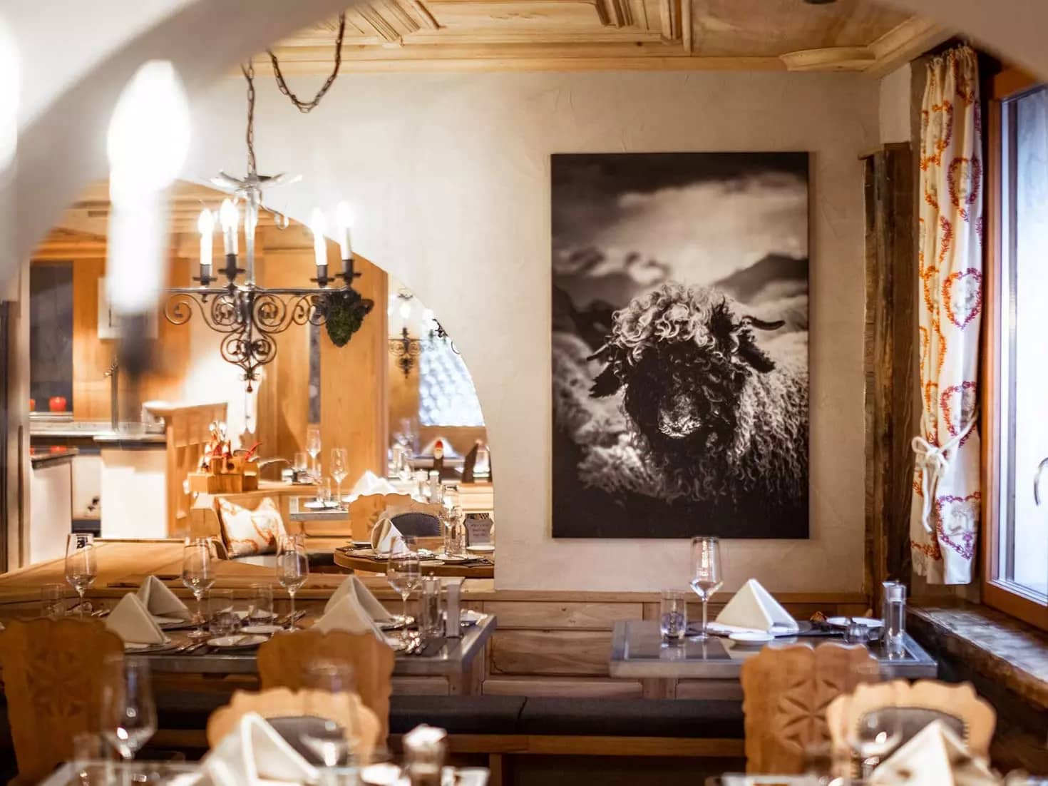 Restaurant interior with wooden tables, chandeliers, and a large black and white sheep wall art