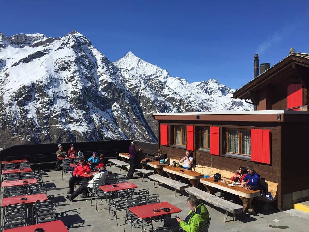 People dining on outdoor restaurant terrace with snow-covered alpine mountains