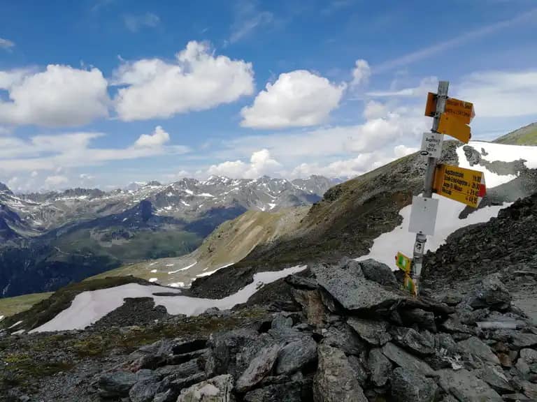Augstbordpass hiking trail sign with mountain peaks and snow in the Swiss Alps