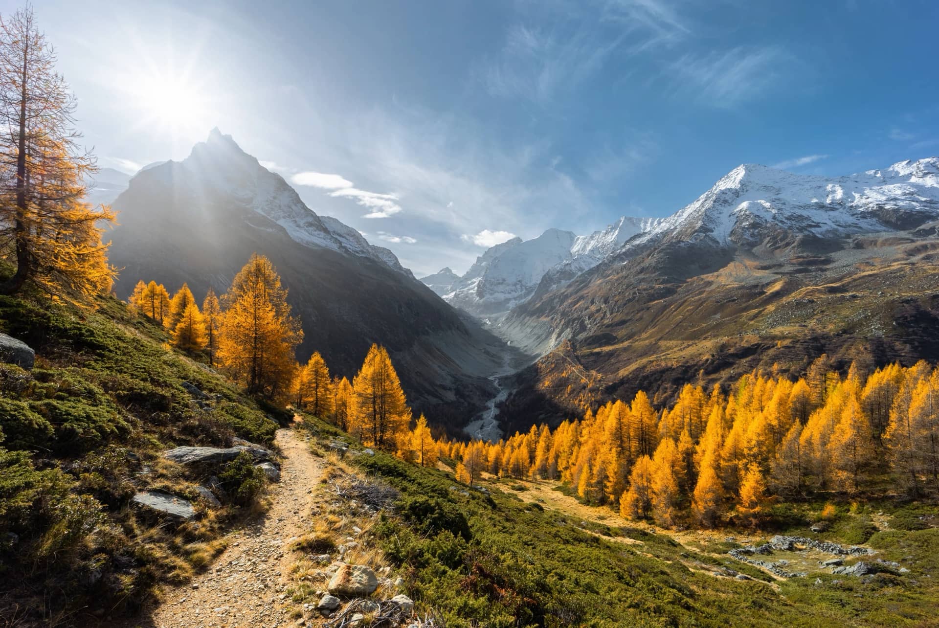 Landscape view on the Zinal valley with a sunburst illuminating the golden larch trees