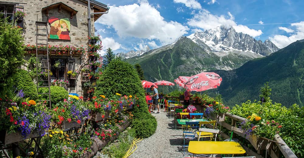 Outdoor cafe terrace with colorful tables and floral decoration overlooking alpine mountain peaks with snow