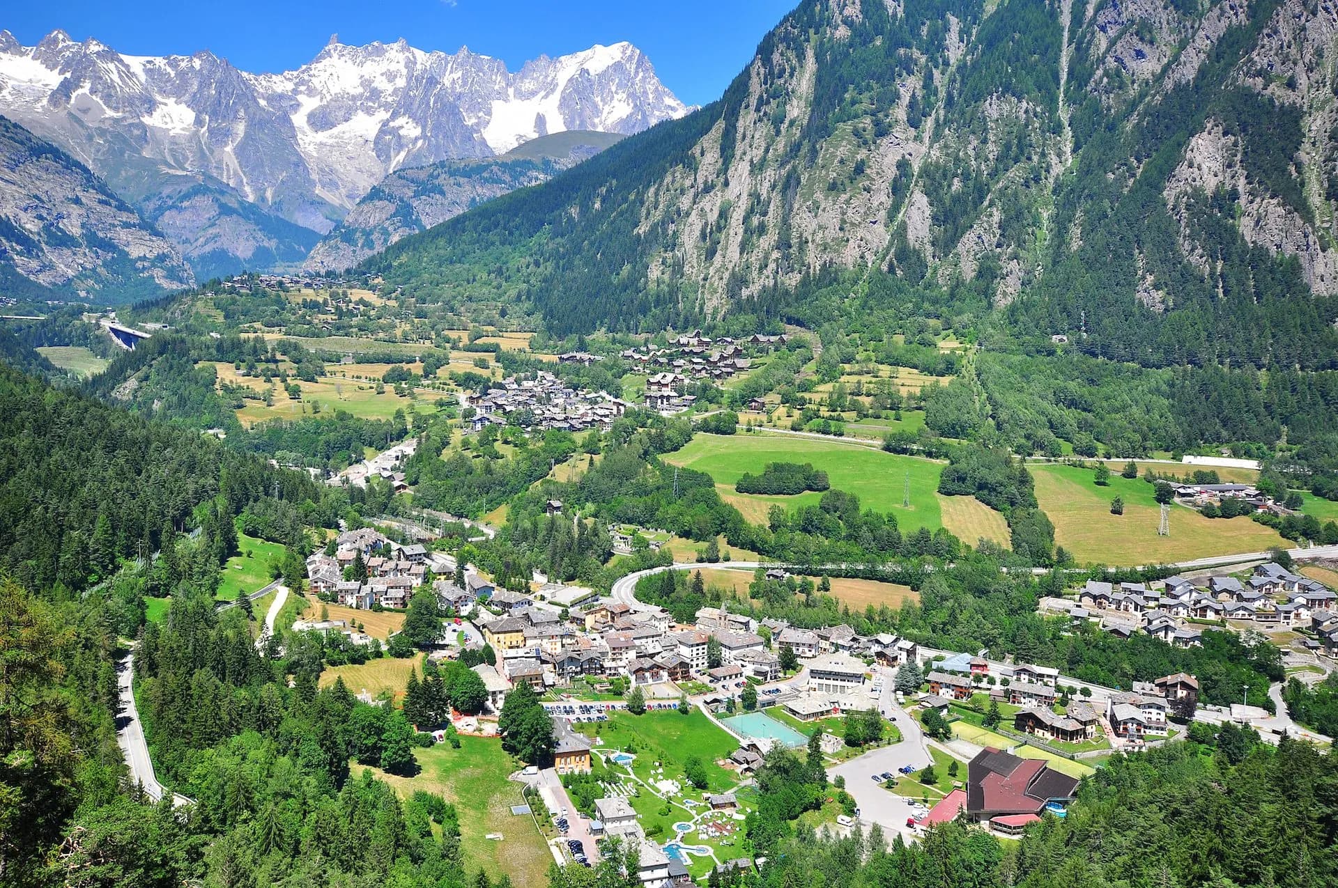 Alpine village nestled in green valley below snow-capped mountains in Courmayeur.