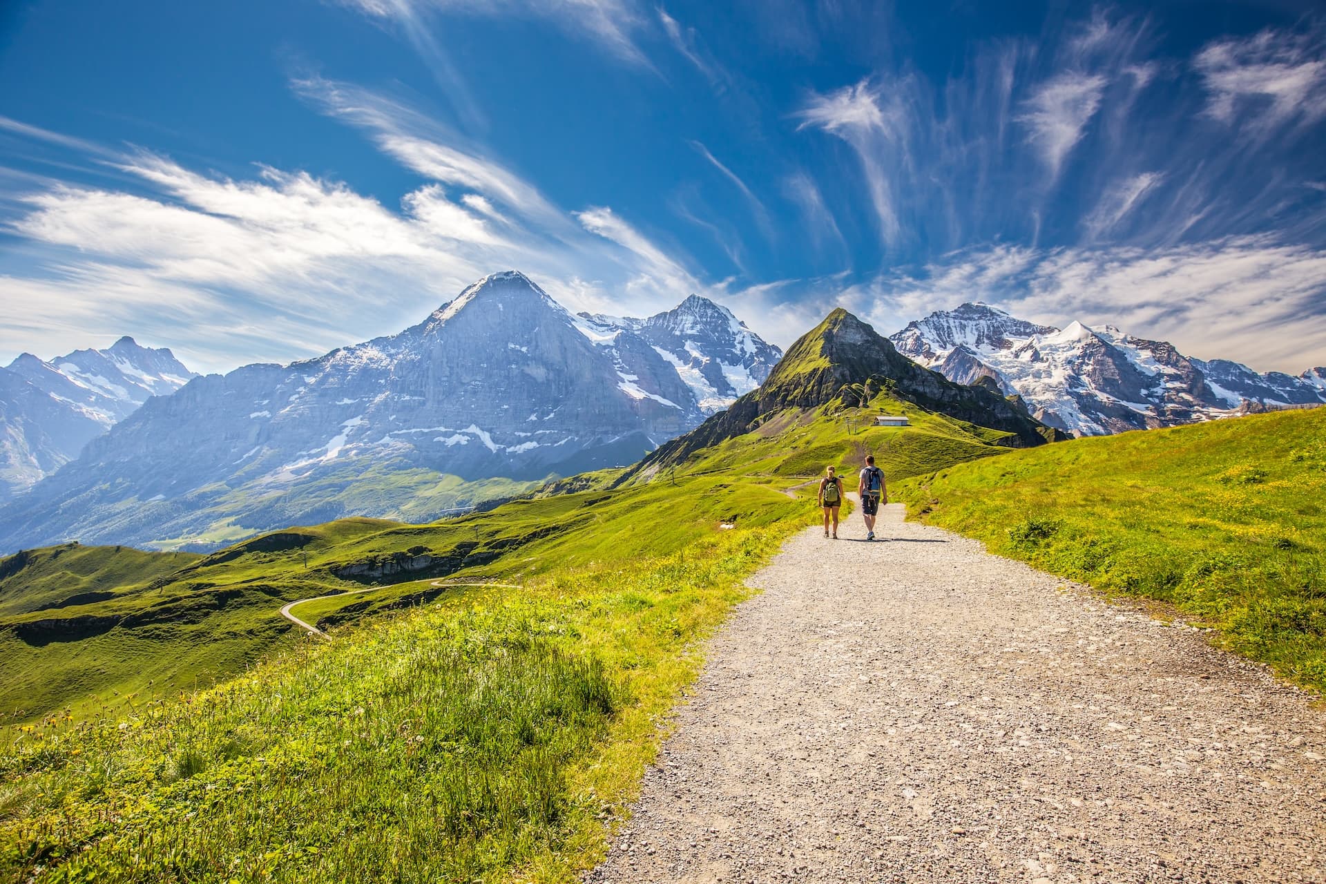 Hiking on a gravel path through green alpine meadows toward snow-capped mountains in Switzerland.