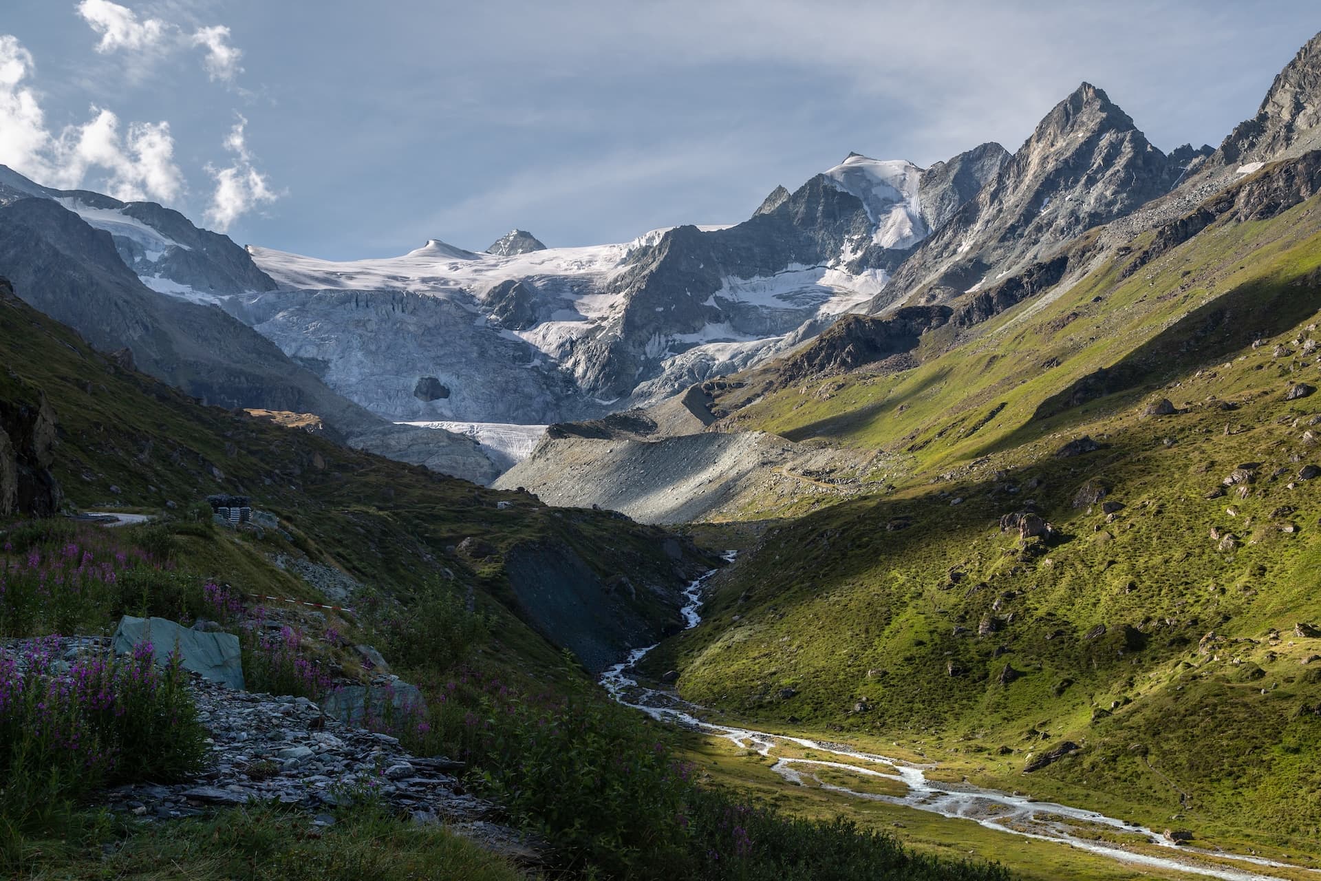 Glacier de Moiry in Switzerland with steep green slopes and a glacial meltwater stream.