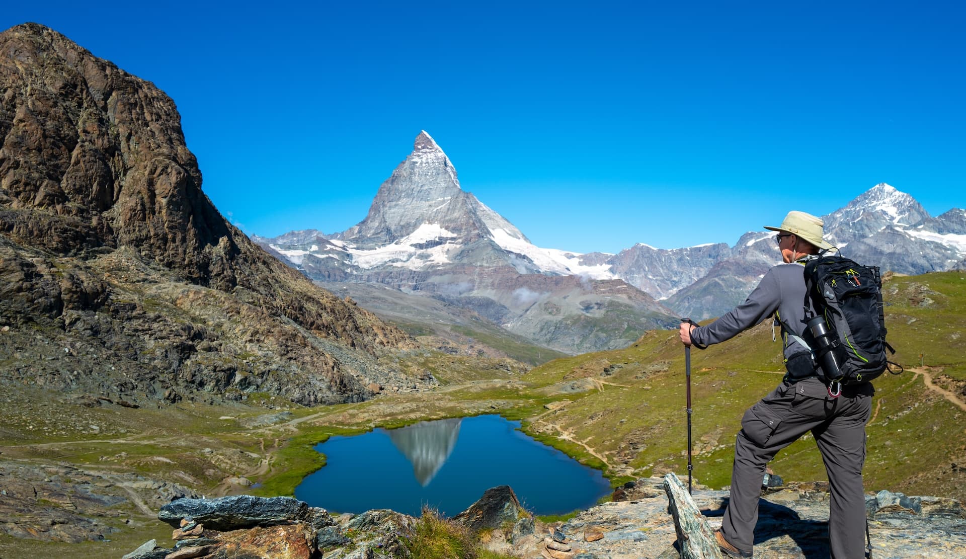 Hiker overlooking Matterhorn reflection in alpine lake from Five Lake Trail.