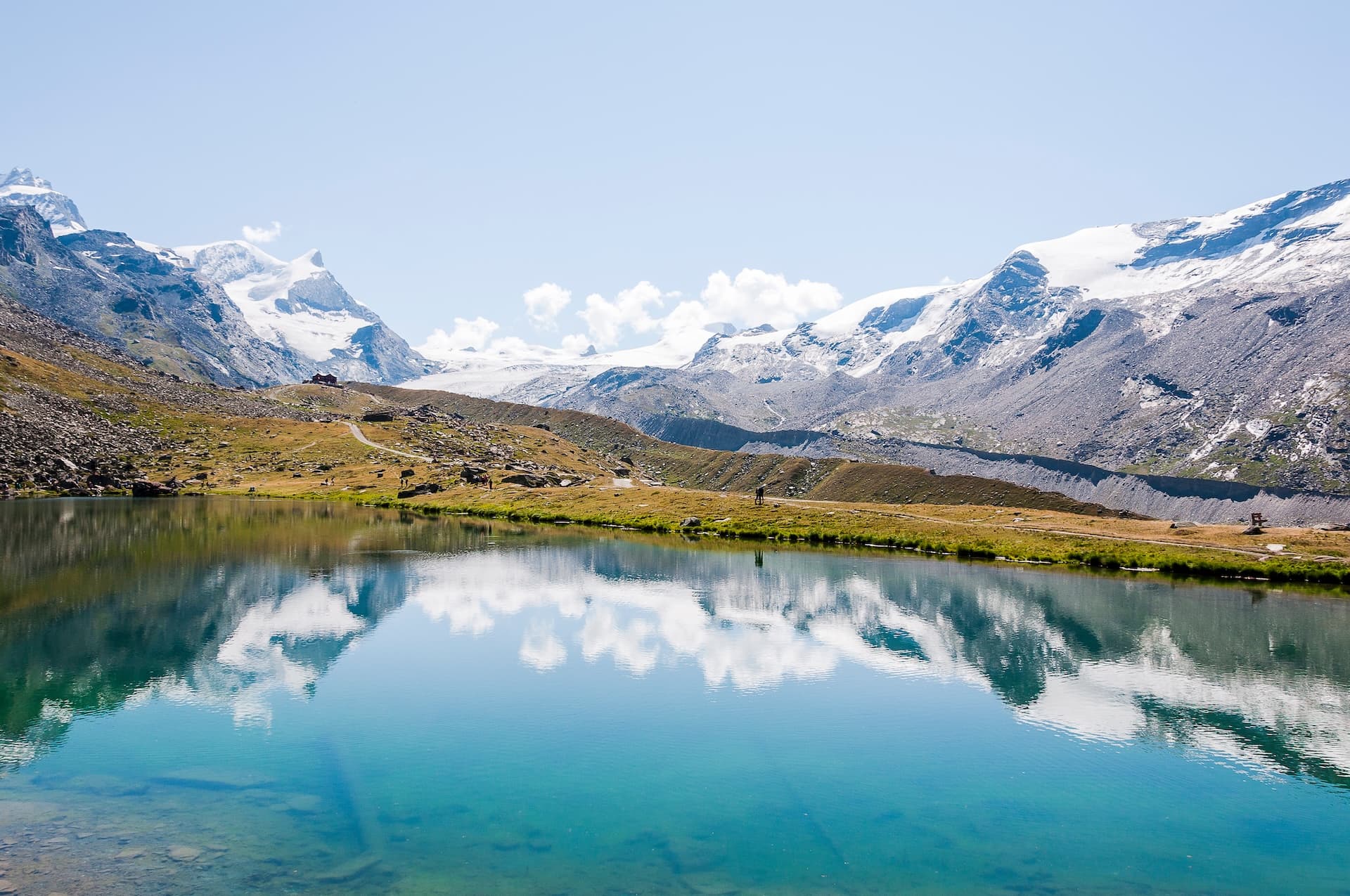 Alpine lake reflecting snow-capped mountains and blue sky, Stellisee, Switzerland.