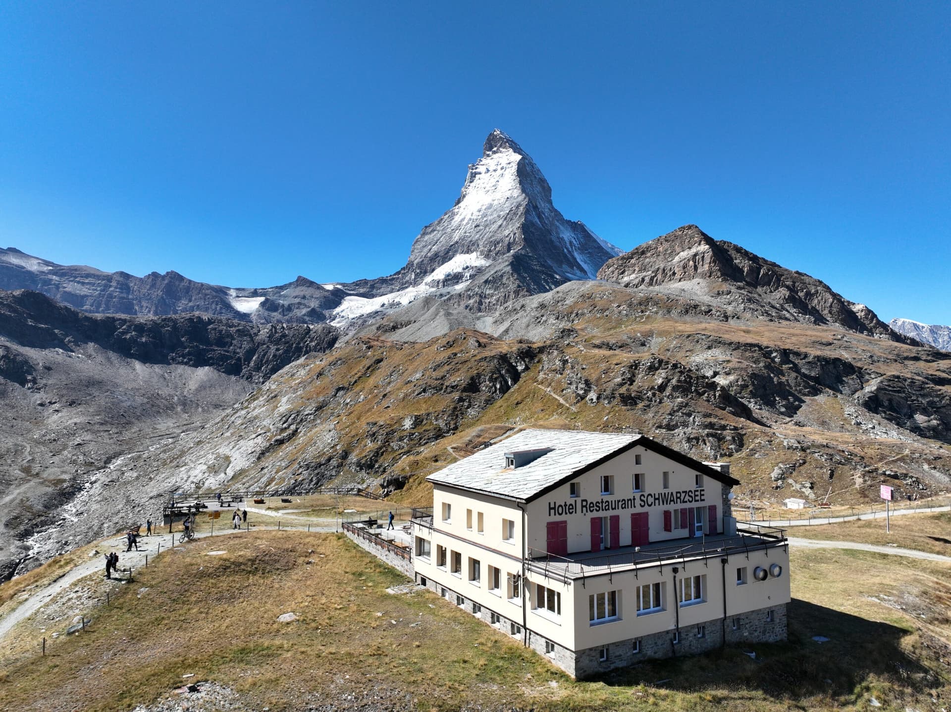Hotel Restaurant Schwarzsee with snow-capped Matterhorn peak in the background under a clear blue sky.