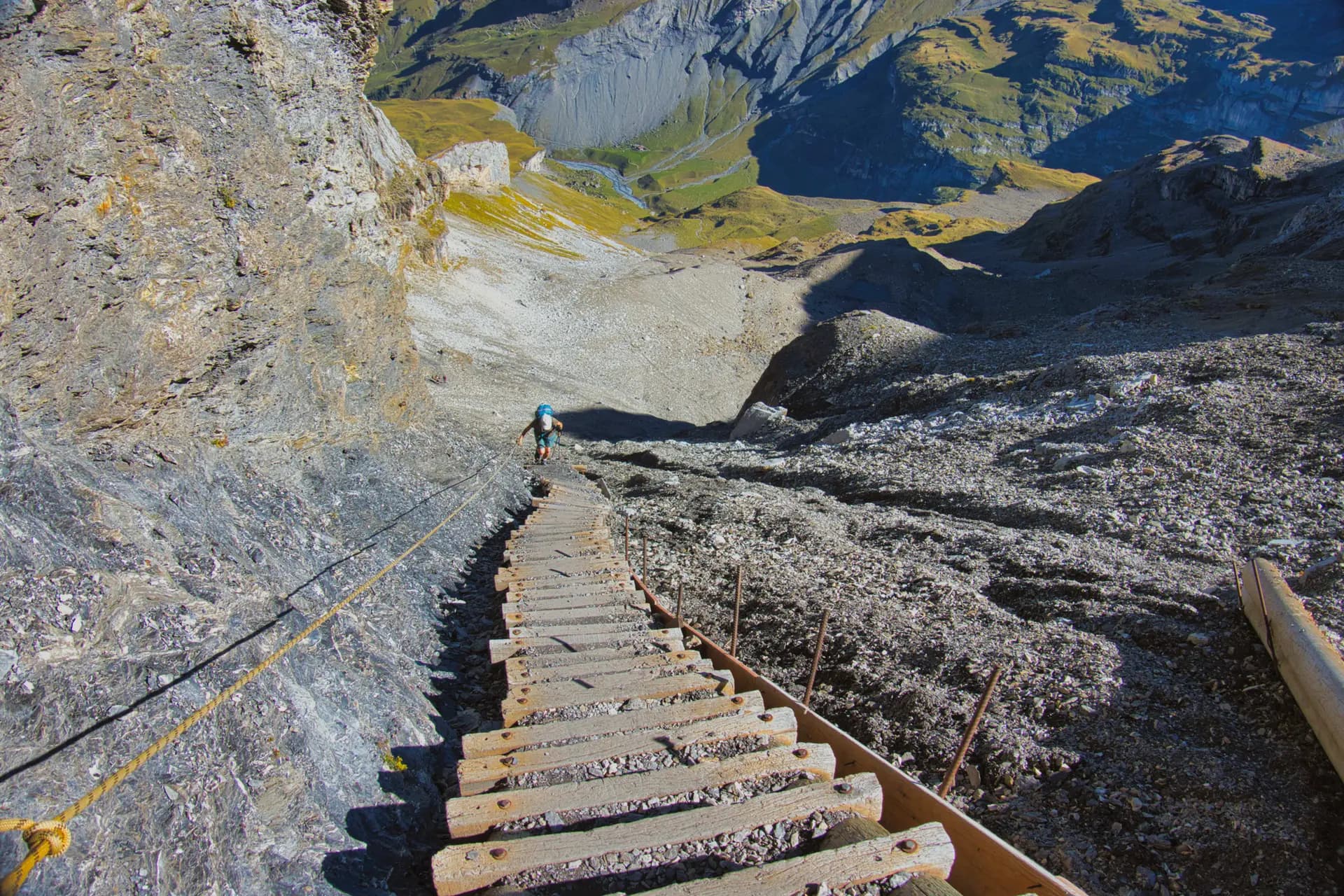 Hiker descending steep wooden stairs on a rocky mountain trail with a safety rope.