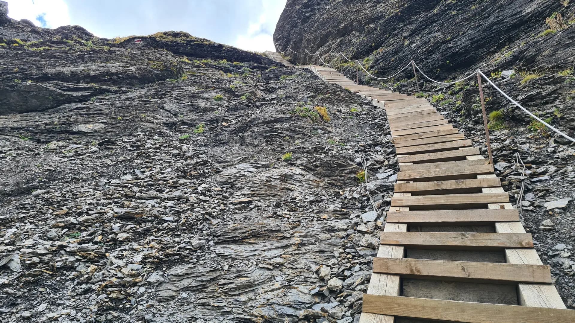 Wooden staircase on a steep, rocky mountain hiking trail with a rope handrail.