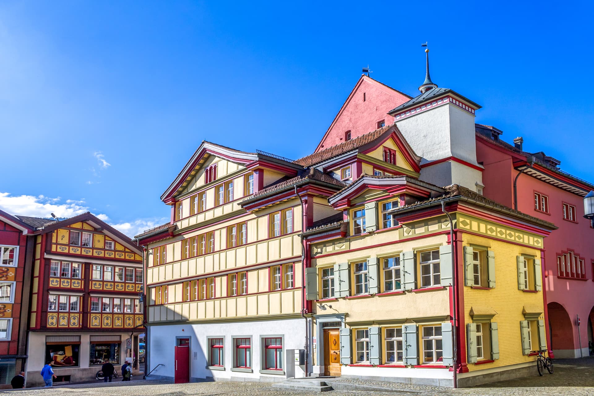 Colorful historic buildings on a cobblestone square under a bright blue sky in Appenzell town.