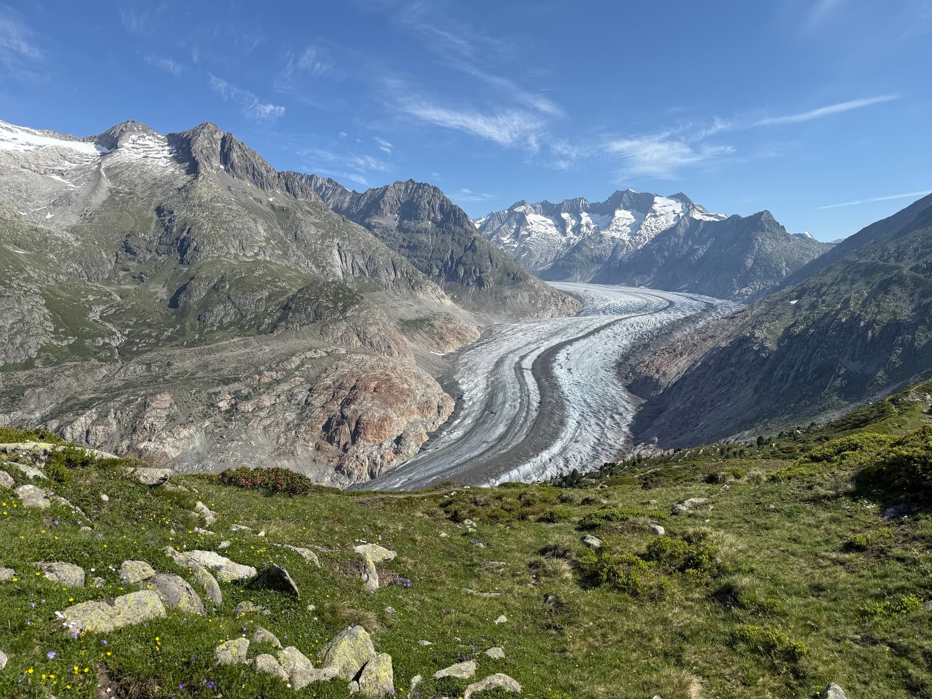 Large glacier curving through an alpine mountain valley under a blue sky