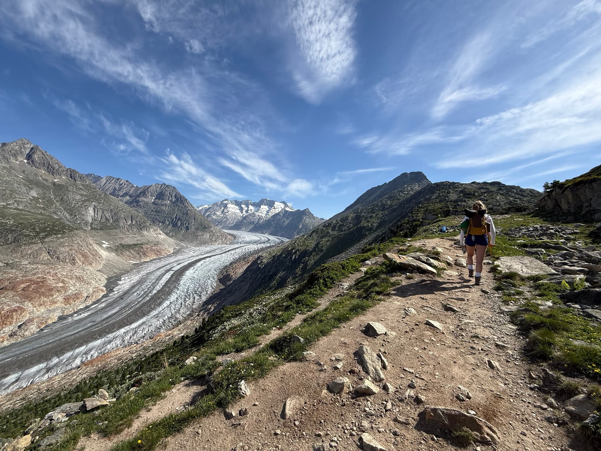 Hiker on mountain ridge trail overlooking large glacier and alpine peaks