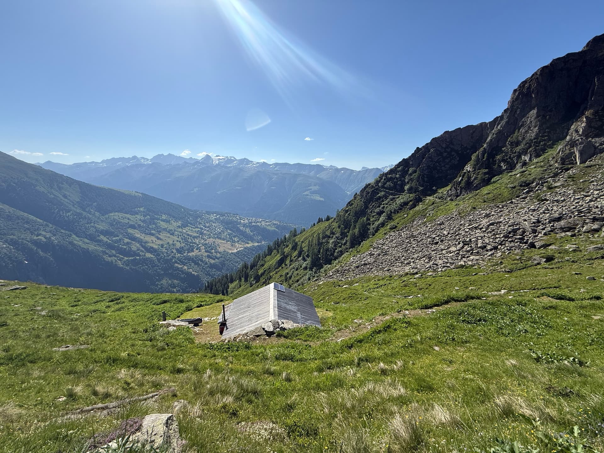 Stone hut on steep alpine pasture with mountain peaks and bright sun