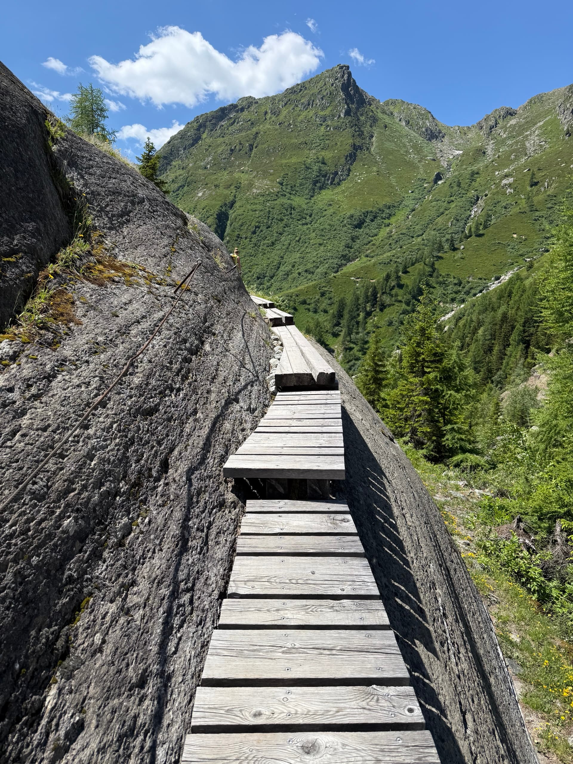 Wooden walkway along a rocky cliff with mountain backdrop