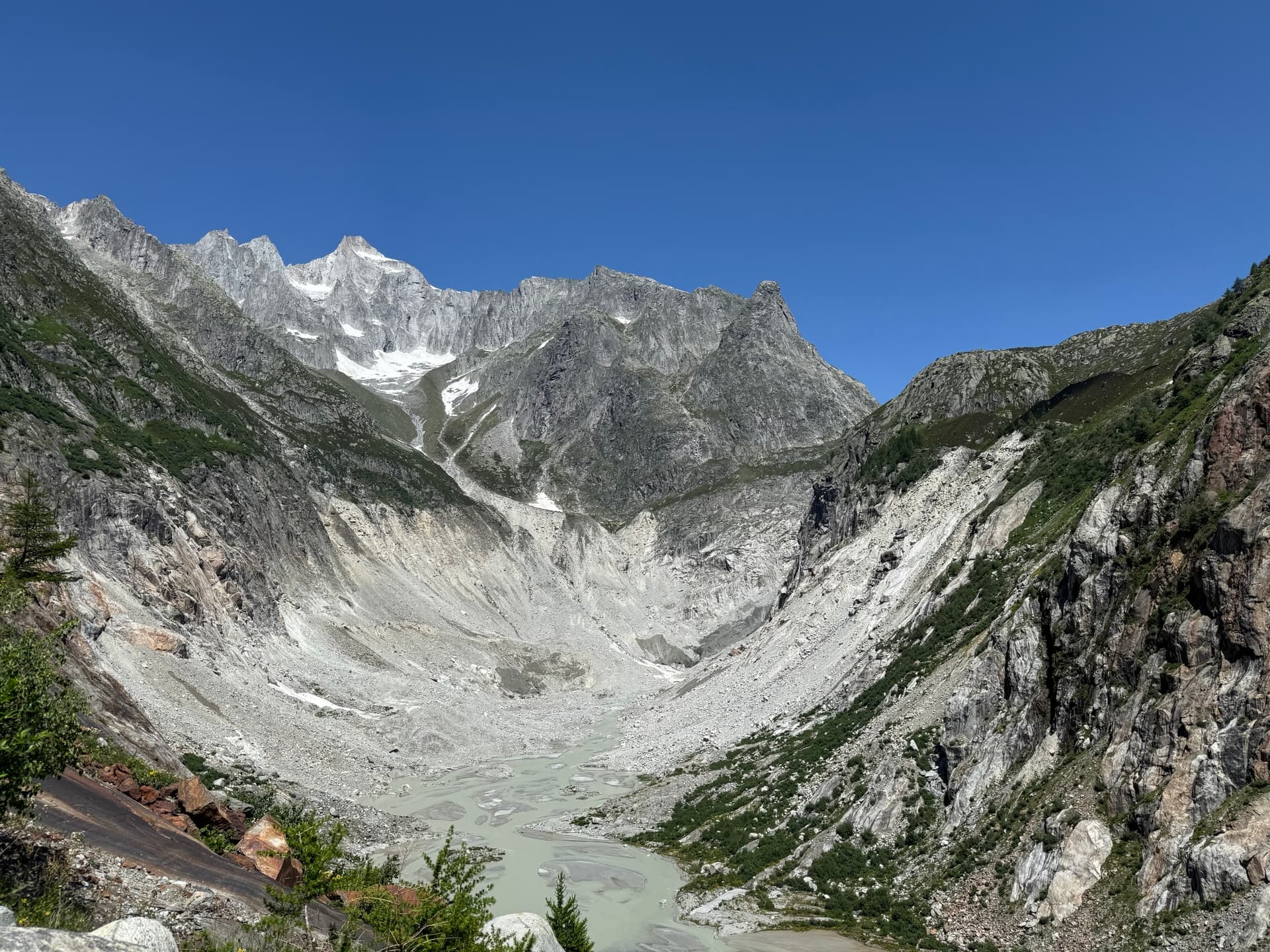 Glacial valley with milky river and rocky mountain peaks under blue sky
