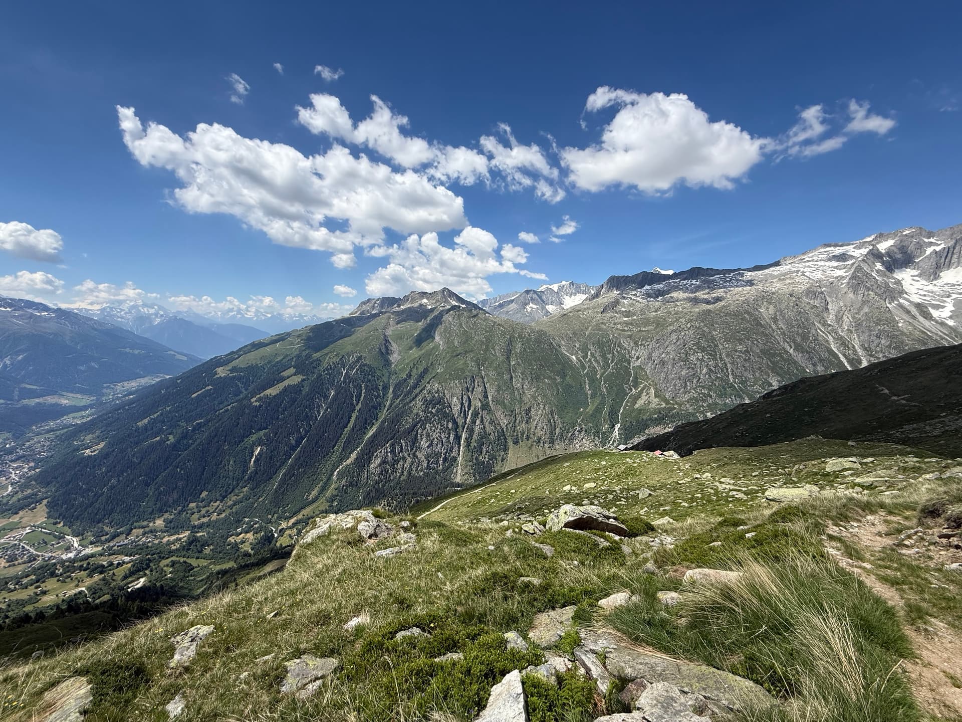 Wide view of alpine valley with snowy mountain peaks under blue sky with white clouds