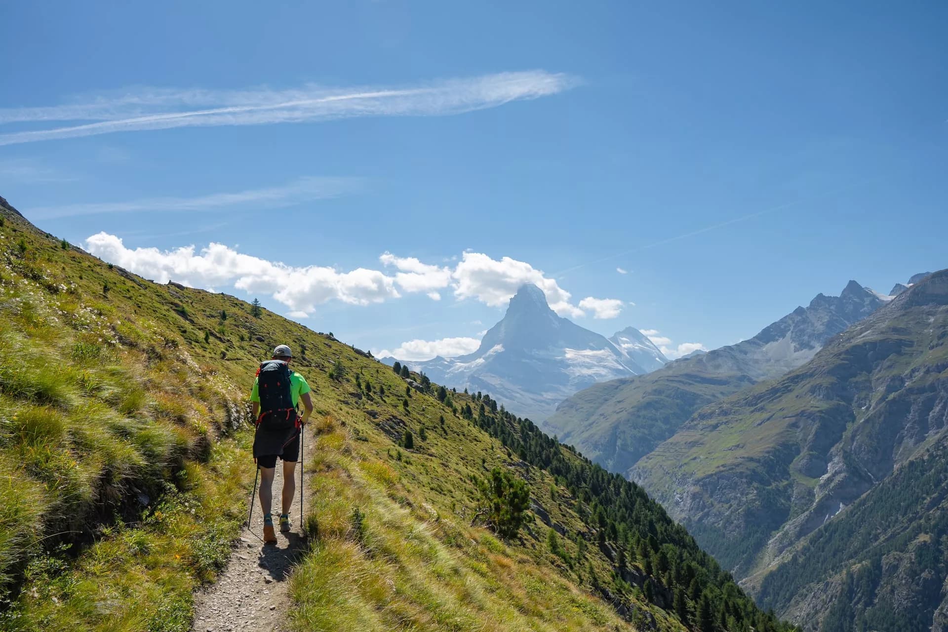 Hiker with poles on grassy trail overlooking Matterhorn mountain in Swiss Alps