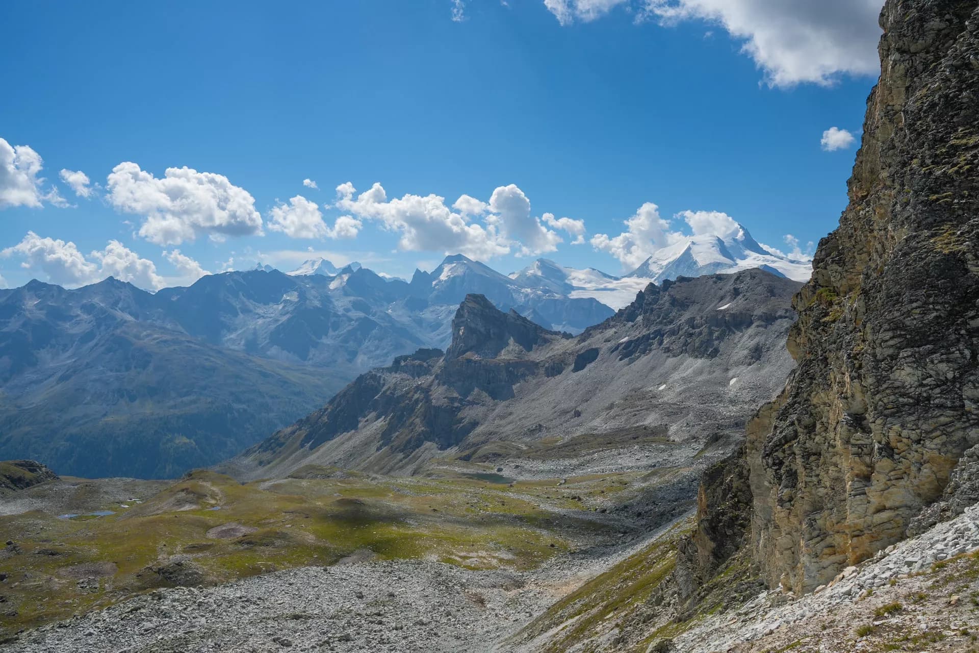 Mountain landscape from Meidpass with rocky foreground, distant snow-capped peaks, and blue sky.