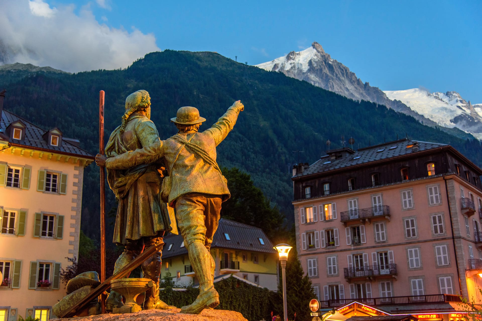 Chamonix bronze statues pointing toward snow-covered mountain peaks with alpine buildings