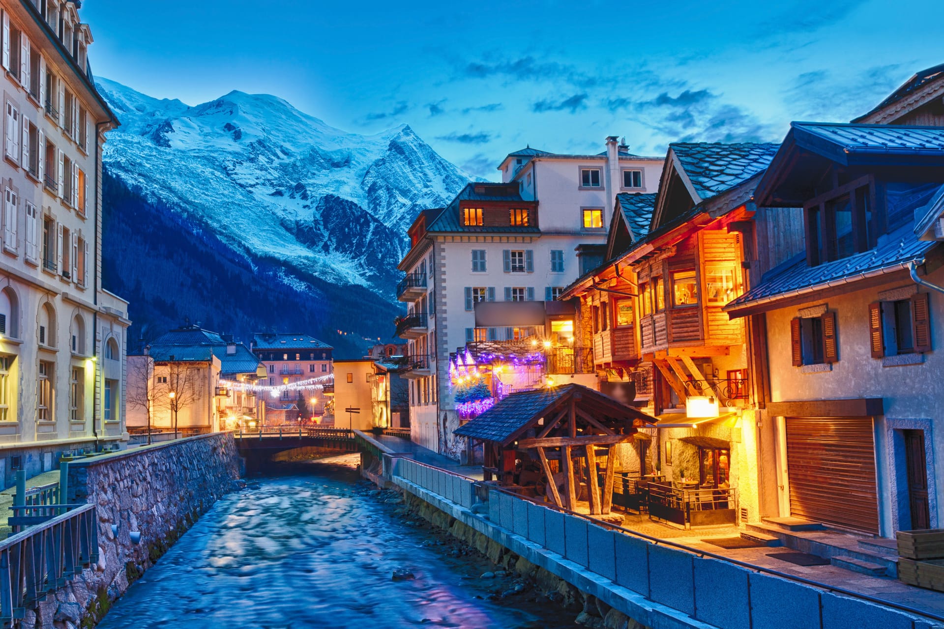 Chamonix alpine village buildings along a river with snowy mountains at dusk
