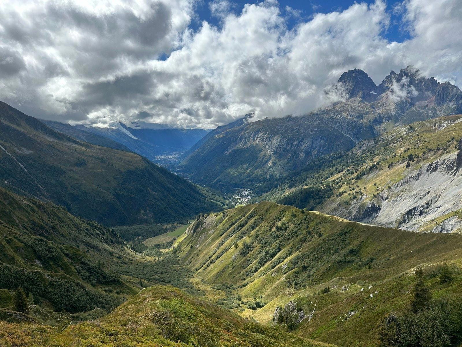 Alpine mountain valley with dramatic peaks, green slopes, and cloudy sky