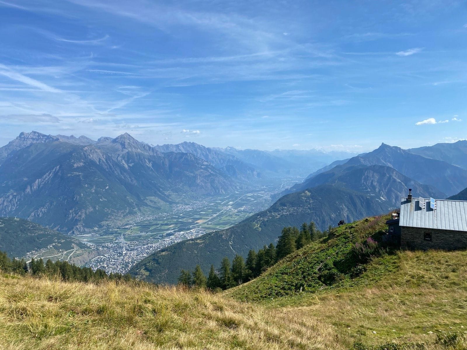 Alpine mountain valley view with distant town and cabin on hillside slope