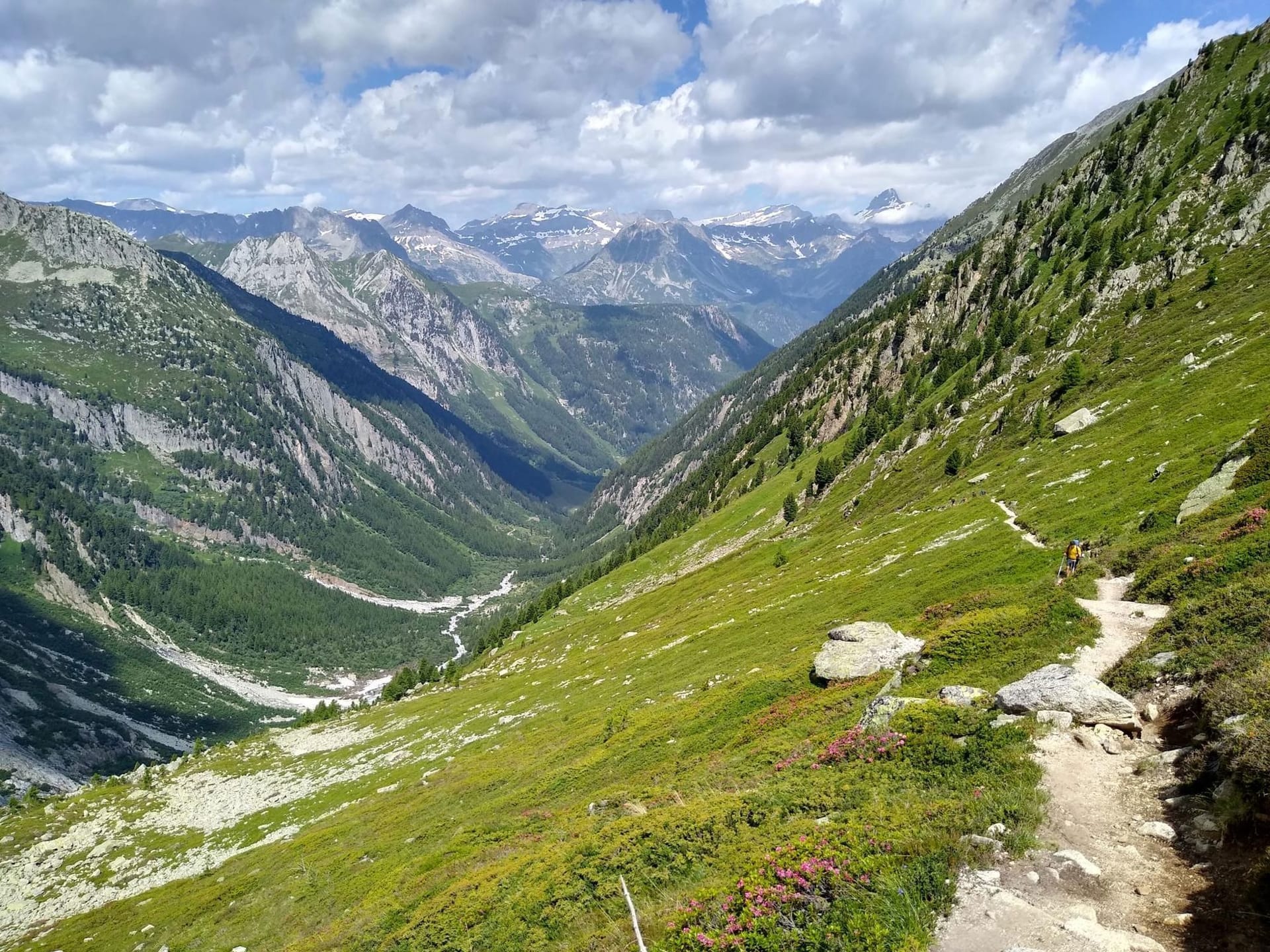 Hiking trail descending into a green alpine valley with snow-capped mountain peaks in Fen Tre D'Arpette