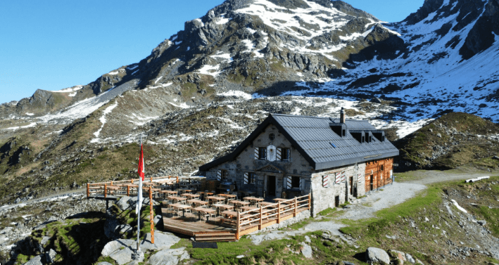 Mountain chalet with outdoor dining terrace in front of snow-covered alpine peaks