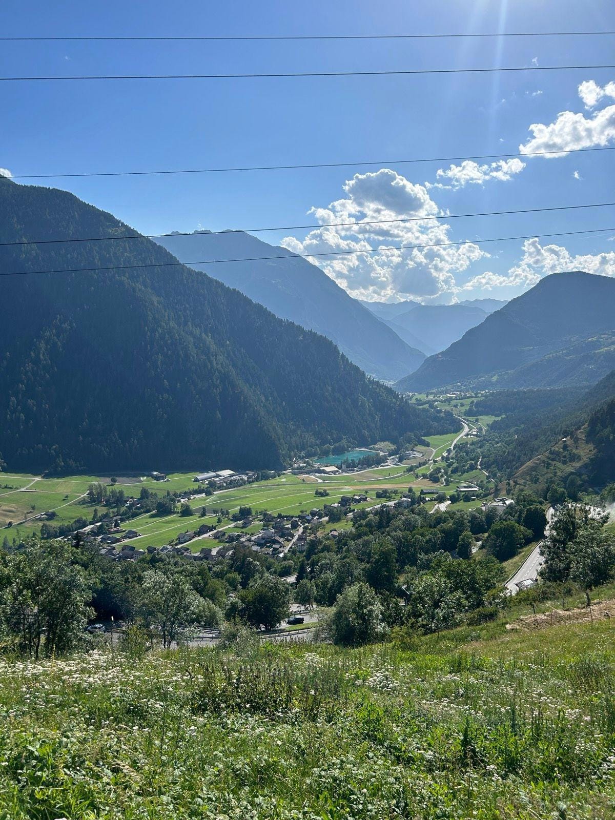 Alpine valley village surrounded by steep green mountains under a blue sky with clouds