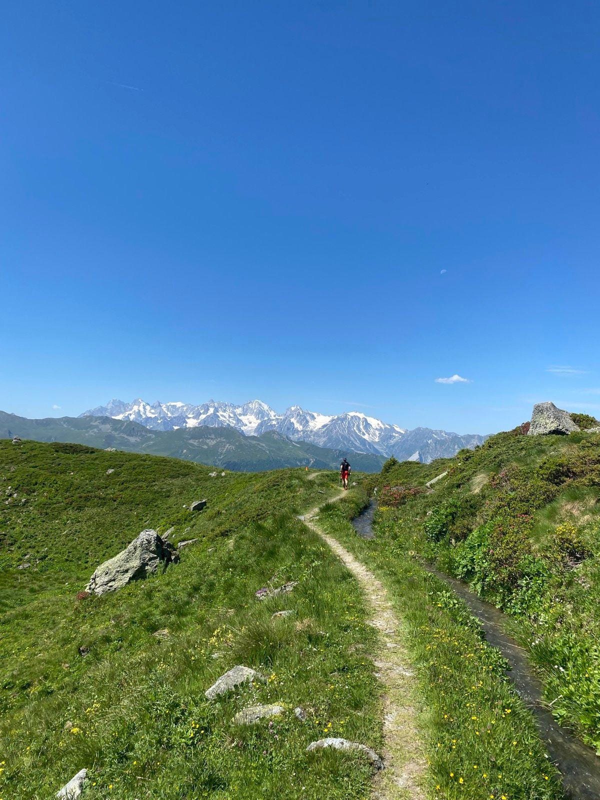 Hiker on alpine trail with snow-capped mountain range in background under blue sky