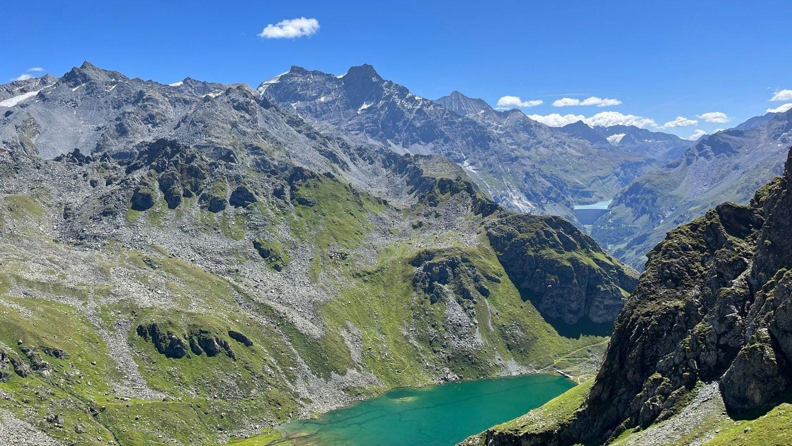 Alpine mountain peaks with green valley lake under a blue sky