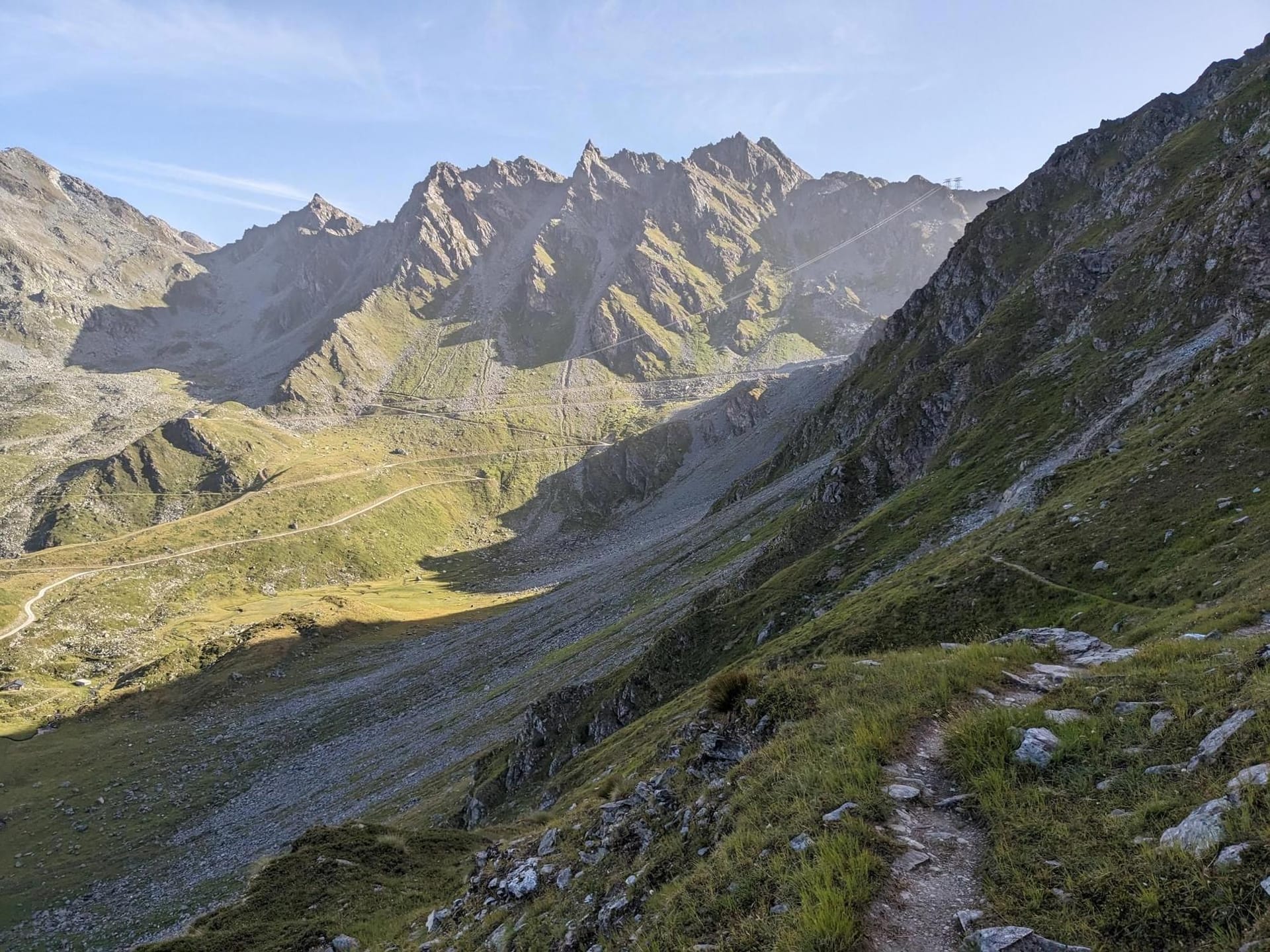 Alpine mountain valley with rocky peaks, grassy slopes, and a winding dirt trail