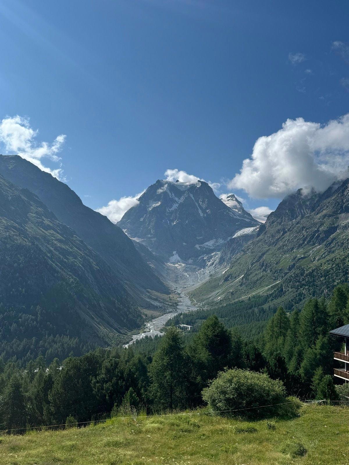 Alpine mountain valley with snow-capped peaks, river, and pine forest under blue sky