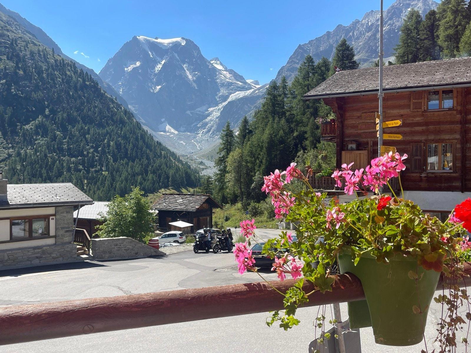 Pink geranium flowers in a pot with Arolla alpine village and snow-capped mountains in the background