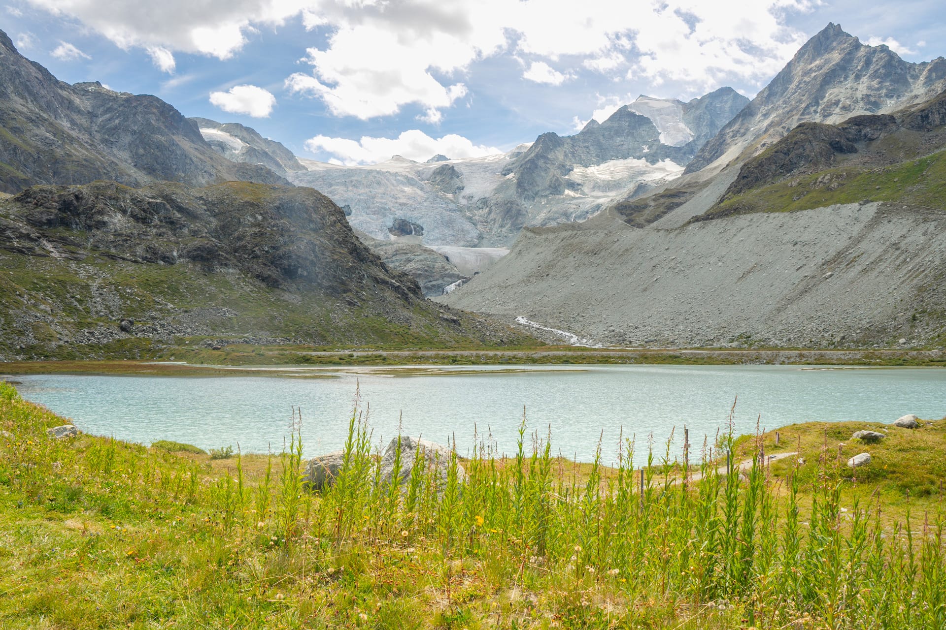 Alpine mountain lake with glacier and rocky peaks under cloudy sky