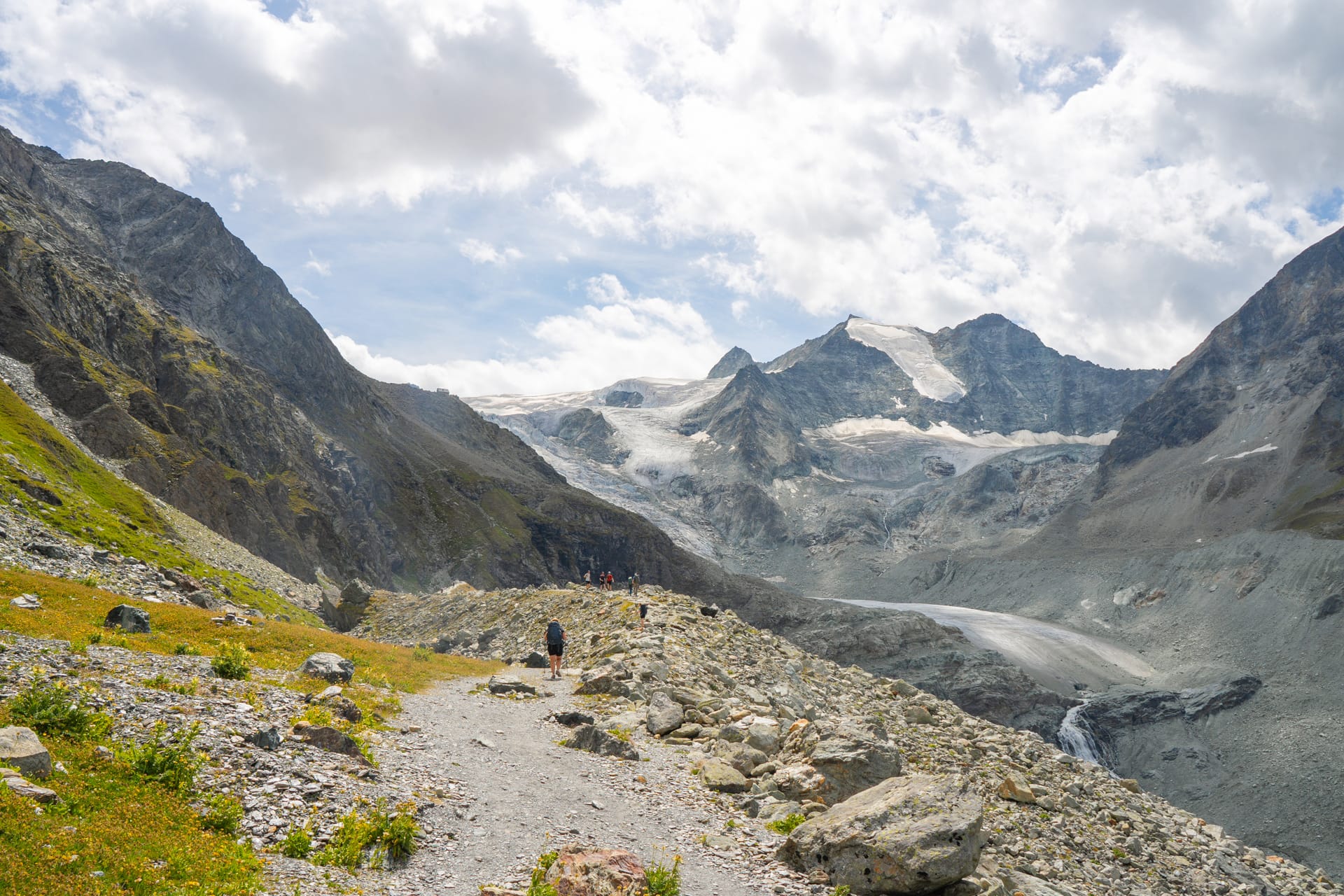 Hikers on a rocky alpine trail with glacier and mountain peaks