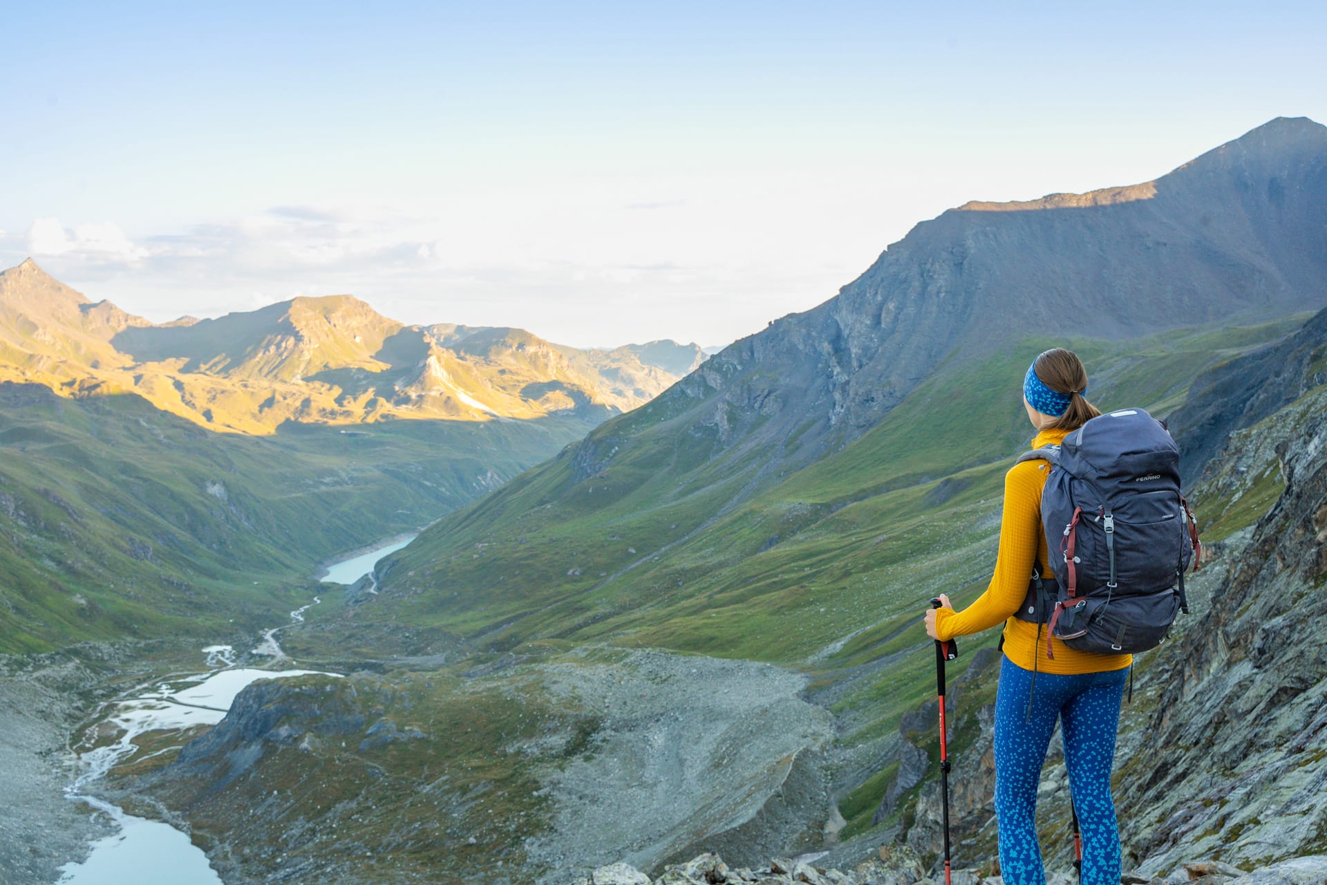 Hiker with backpack and poles looking over alpine mountain valley with lakes