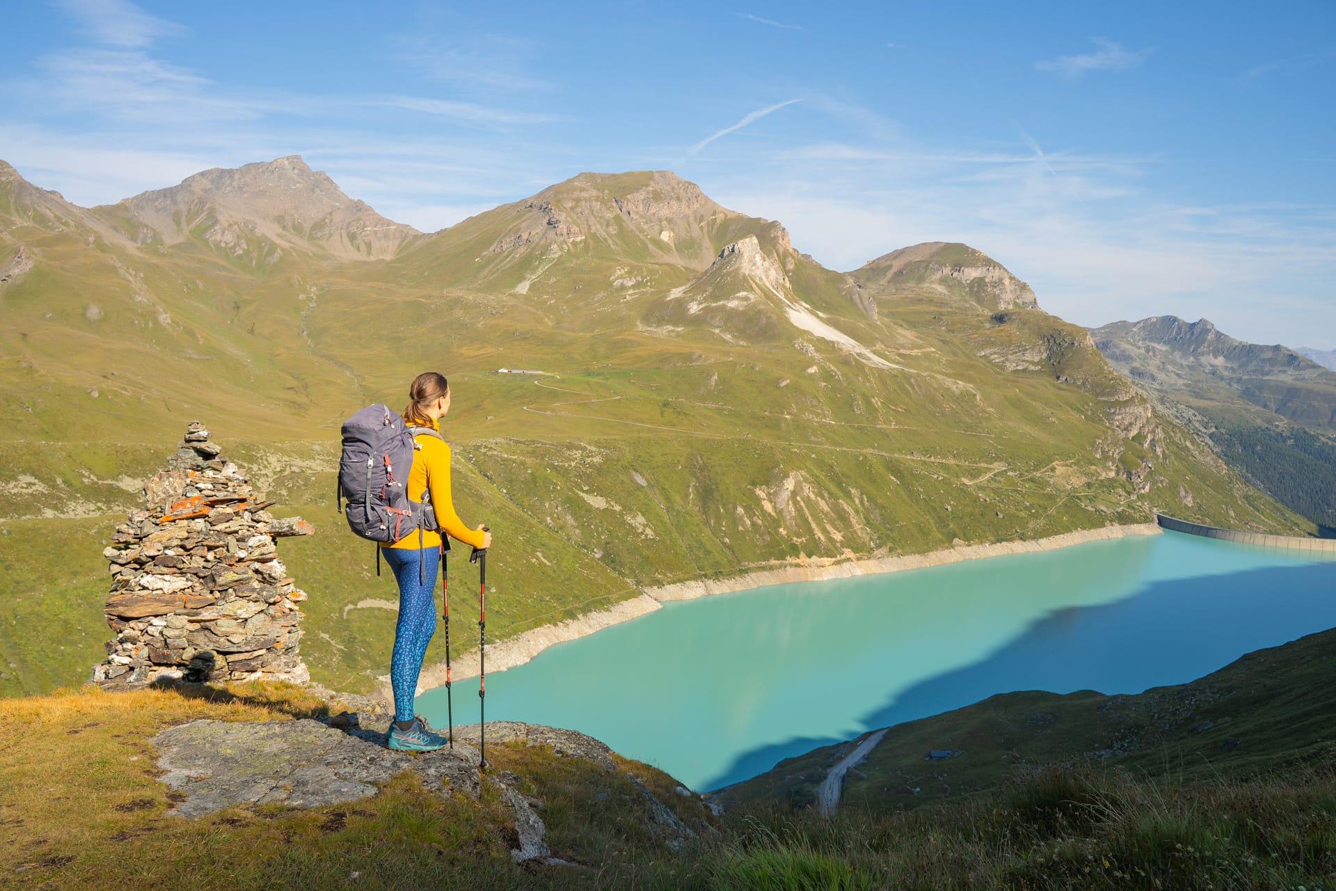 Hiker with backpack and poles standing by alpine reservoir and mountains