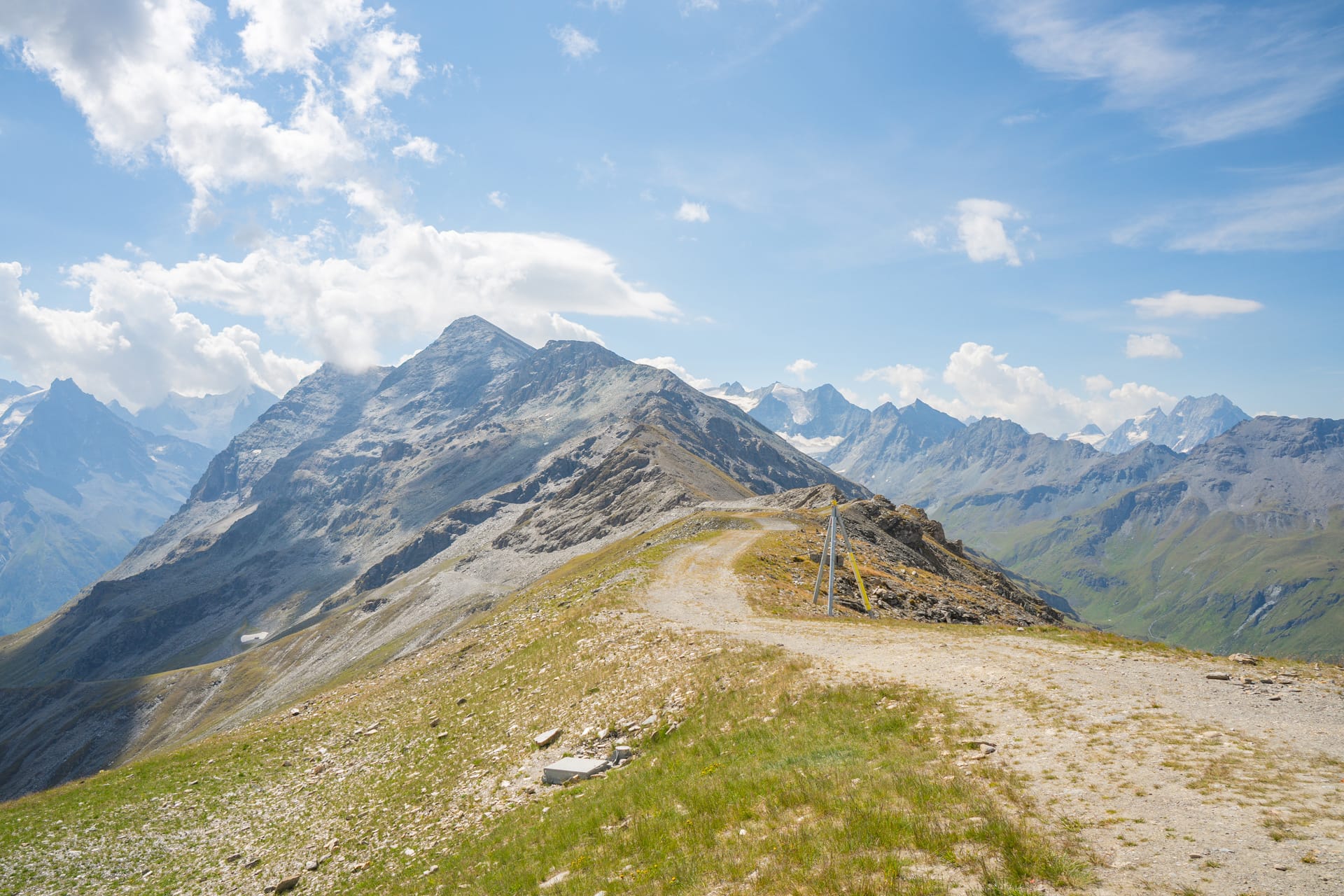 Dirt hiking trail along alpine mountain ridge with panoramic mountain views under a blue sky
